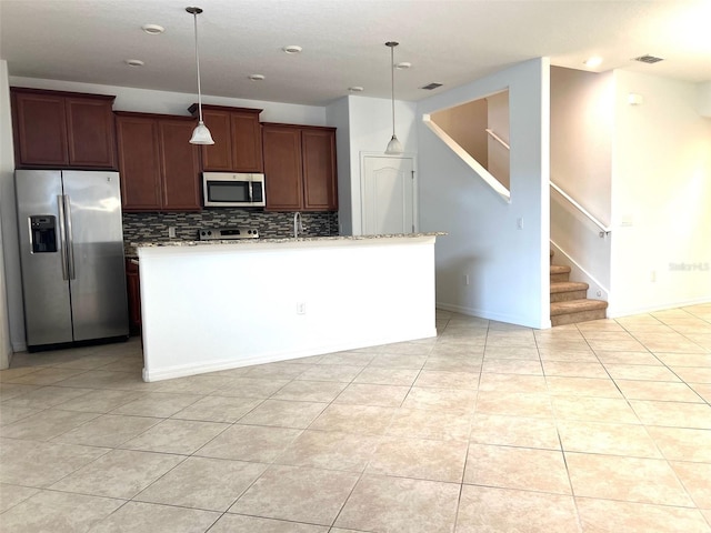 kitchen with an island with sink, appliances with stainless steel finishes, light countertops, and pendant lighting