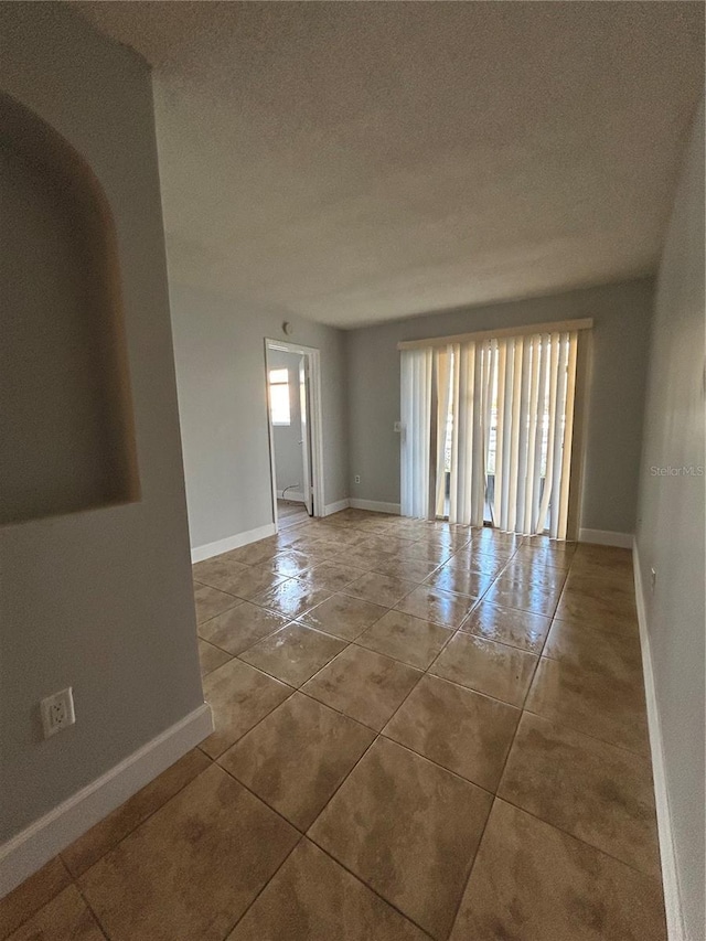 unfurnished room featuring a textured ceiling, tile patterned floors, and baseboards