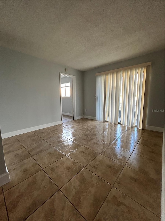 unfurnished room with a textured ceiling, baseboards, and dark tile patterned floors