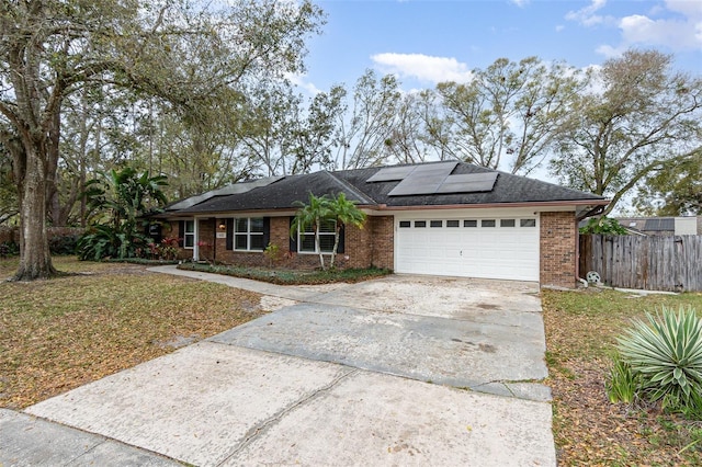 single story home with brick siding, solar panels, concrete driveway, fence, and a garage