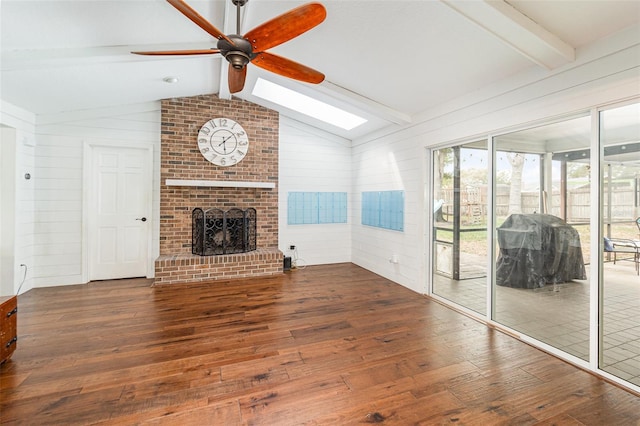 unfurnished living room with ceiling fan, vaulted ceiling with skylight, wooden walls, a brick fireplace, and wood-type flooring