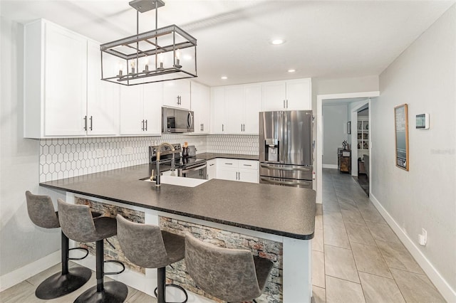 kitchen featuring decorative backsplash, dark countertops, appliances with stainless steel finishes, a peninsula, and white cabinetry