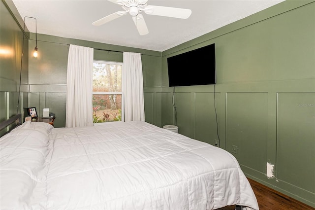 bedroom featuring dark wood-style floors, a decorative wall, and a ceiling fan