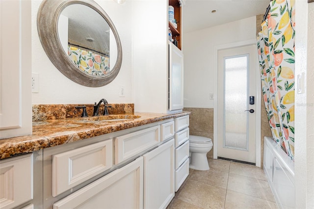 full bath with toilet, a wainscoted wall, tile walls, vanity, and tile patterned floors