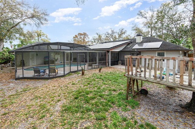 rear view of property featuring a chimney, solar panels, a patio area, a deck, and an outdoor pool