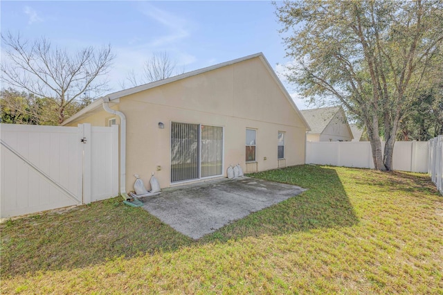 rear view of property featuring a fenced backyard, a gate, a yard, a patio area, and stucco siding