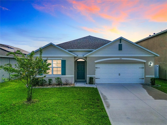 ranch-style home featuring roof with shingles, a lawn, concrete driveway, and stucco siding