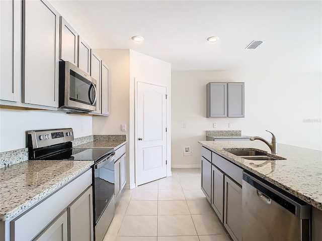 kitchen featuring light tile patterned floors, light stone counters, gray cabinets, stainless steel appliances, and a sink