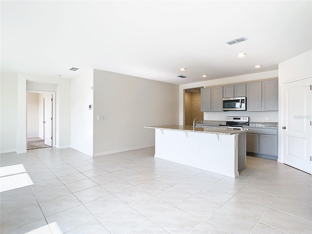 kitchen featuring a center island with sink, gray cabinets, visible vents, appliances with stainless steel finishes, and stone countertops