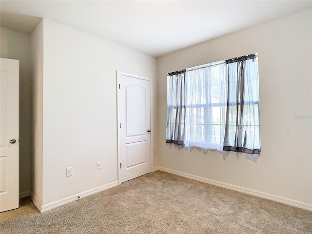 spare room with baseboards and light colored carpet