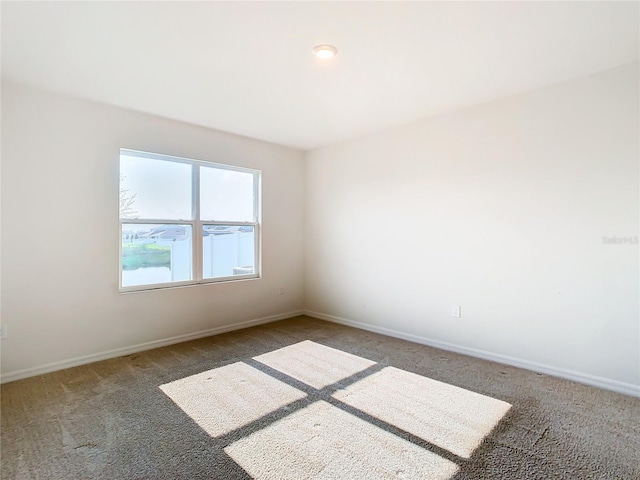 spare room with dark colored carpet and baseboards