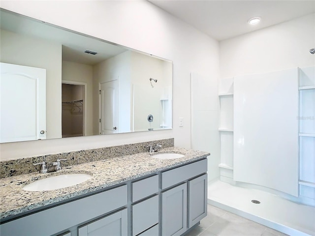 bathroom featuring a spacious closet, double vanity, a stall shower, and a sink