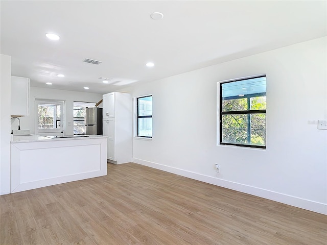 kitchen with light hardwood / wood-style flooring, stainless steel refrigerator, cooktop, sink, and white cabinets