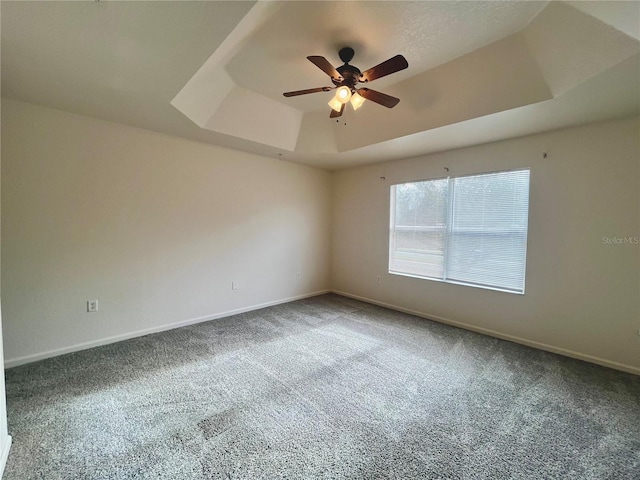 carpeted empty room featuring a raised ceiling, ceiling fan, and baseboards