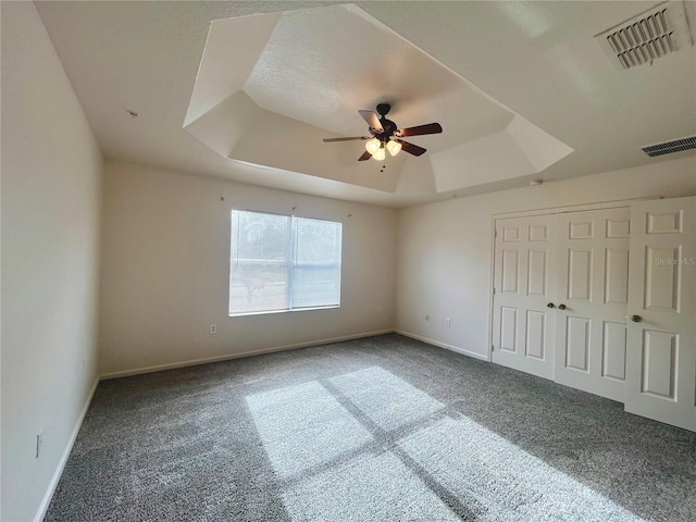 unfurnished bedroom with carpet floors, a raised ceiling, visible vents, and baseboards