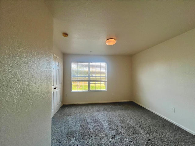 empty room with baseboards, dark carpet, and a textured wall