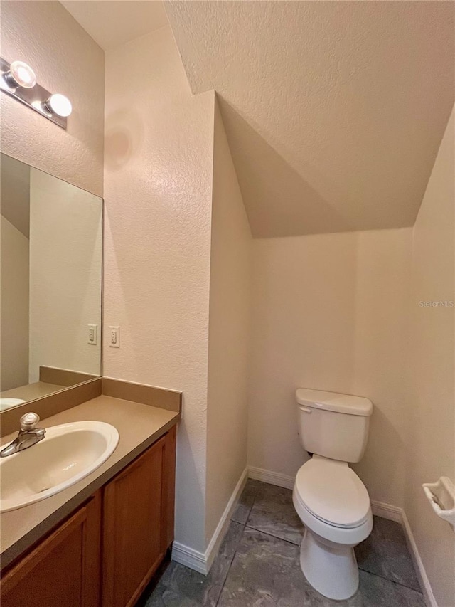 half bathroom with lofted ceiling, baseboards, vanity, and toilet