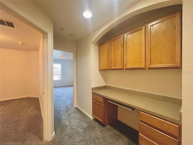 unfurnished office featuring baseboards, visible vents, dark carpet, and built in desk