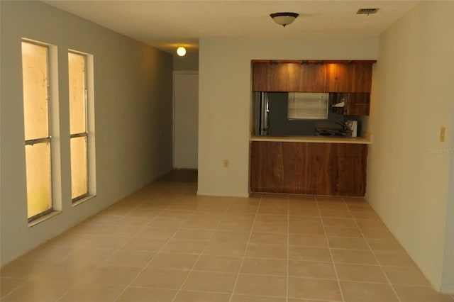 kitchen with visible vents, brown cabinets, freestanding refrigerator, light countertops, and light tile patterned flooring