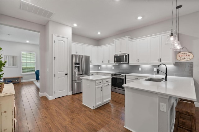 kitchen with hanging light fixtures, a kitchen island, sink, appliances with stainless steel finishes, and white cabinets