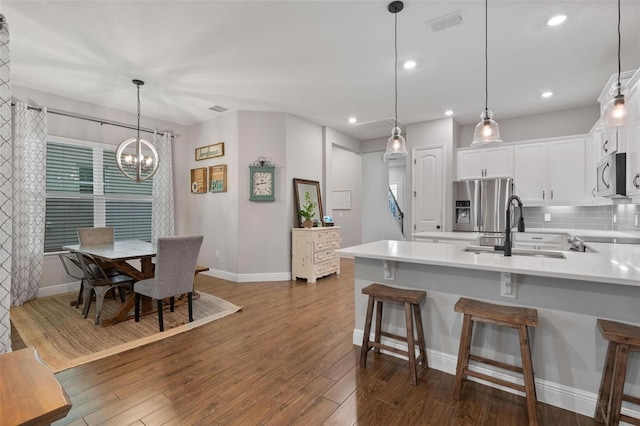 kitchen featuring a kitchen bar, appliances with stainless steel finishes, sink, decorative light fixtures, and white cabinets