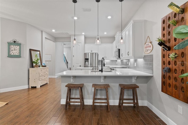 kitchen with white cabinetry, kitchen peninsula, decorative light fixtures, sink, and appliances with stainless steel finishes