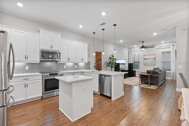 kitchen featuring appliances with stainless steel finishes, white cabinets, pendant lighting, a kitchen island, and kitchen peninsula