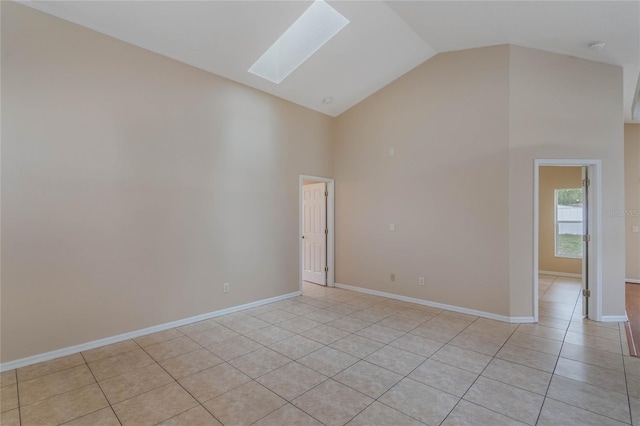 spare room featuring light tile patterned floors, high vaulted ceiling, a skylight, and baseboards