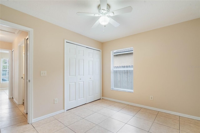 unfurnished bedroom featuring light tile patterned floors, a ceiling fan, baseboards, a closet, and attic access