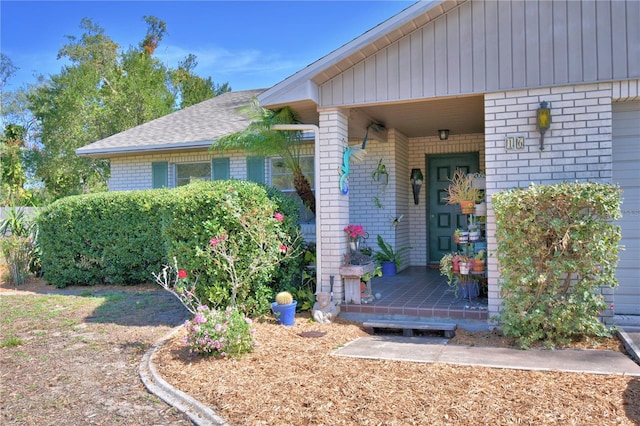 view of exterior entry featuring brick siding and roof with shingles