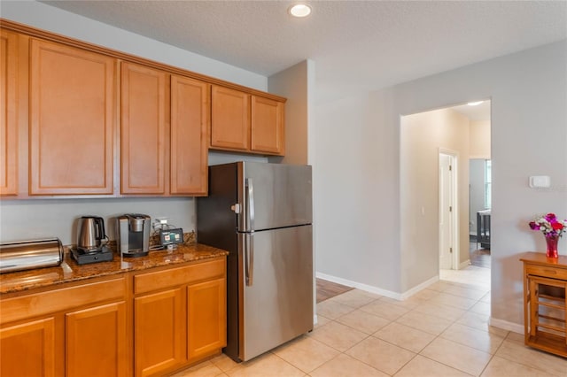 kitchen with light tile patterned floors, baseboards, dark stone countertops, freestanding refrigerator, and a textured ceiling