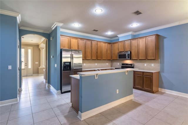 kitchen featuring a center island, backsplash, light tile patterned floors, appliances with stainless steel finishes, and crown molding