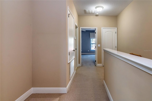 hall with light carpet and a textured ceiling