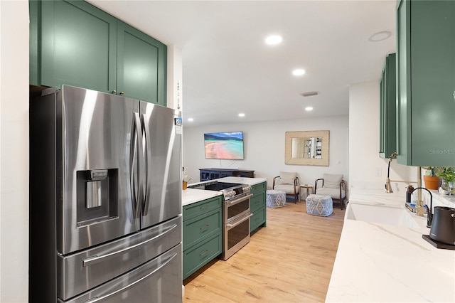 kitchen with green cabinetry, light hardwood / wood-style flooring, light stone countertops, sink, and appliances with stainless steel finishes