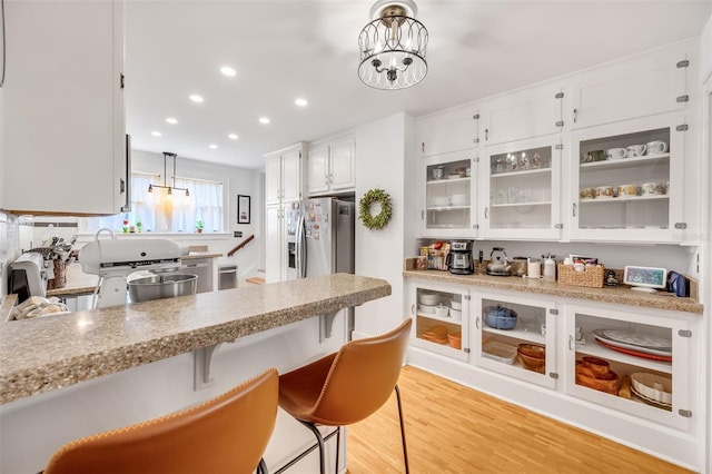 kitchen with decorative light fixtures, glass insert cabinets, white cabinets, light wood-type flooring, and stainless steel fridge