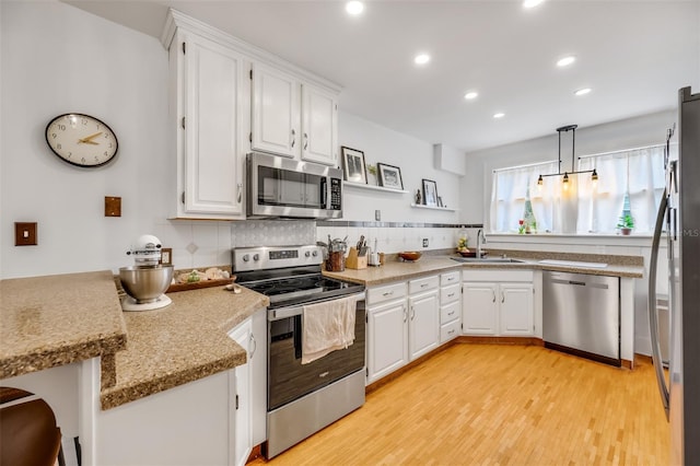 kitchen with a peninsula, a sink, white cabinets, appliances with stainless steel finishes, and decorative backsplash