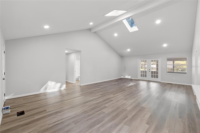 unfurnished living room featuring a skylight, french doors, beam ceiling, light wood-style floors, and baseboards