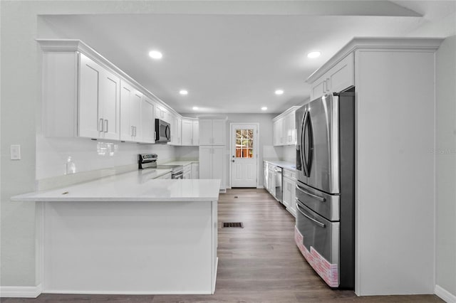 kitchen featuring a peninsula, appliances with stainless steel finishes, white cabinets, and wood finished floors