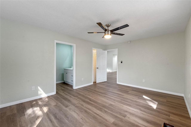 unfurnished bedroom featuring ensuite bath, wood finished floors, a ceiling fan, and baseboards