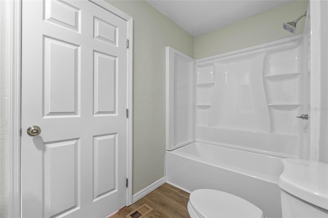 bathroom with toilet, wood finished floors, visible vents, baseboards, and washtub / shower combination