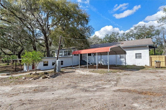 exterior space with dirt driveway, fence, a carport, and brick siding