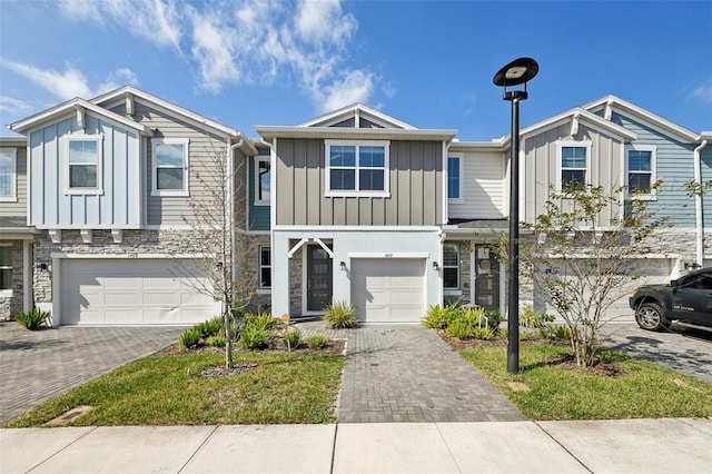 townhome / multi-family property featuring a garage, stone siding, decorative driveway, and board and batten siding