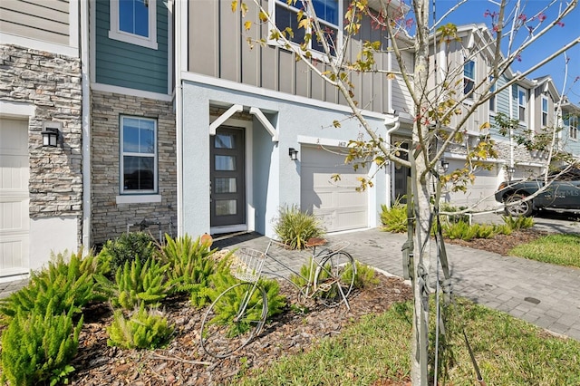 view of exterior entry featuring a garage, stone siding, board and batten siding, and decorative driveway