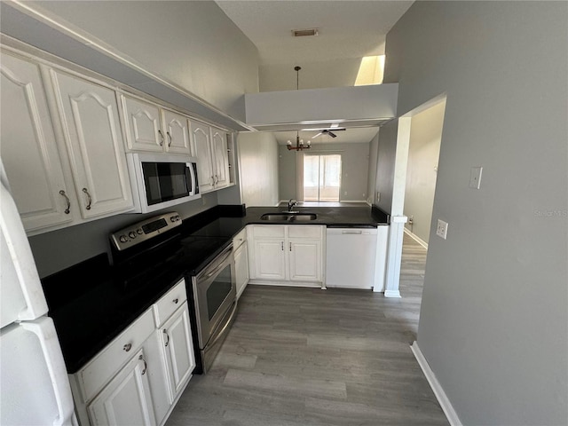 kitchen with dark countertops, white appliances, white cabinetry, and a sink