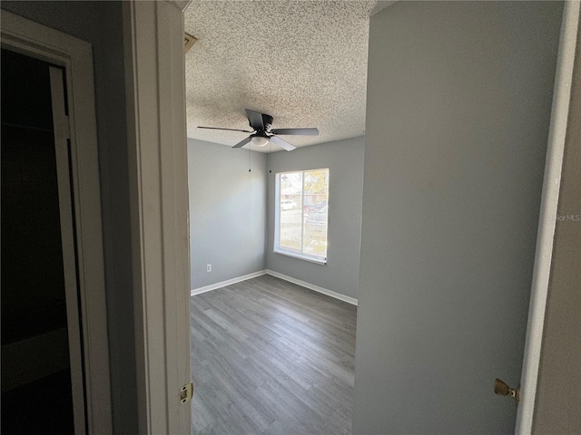 spare room featuring a textured ceiling, ceiling fan, wood finished floors, and baseboards