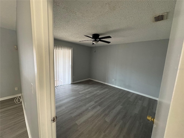 spare room featuring ceiling fan, baseboards, visible vents, and dark wood finished floors