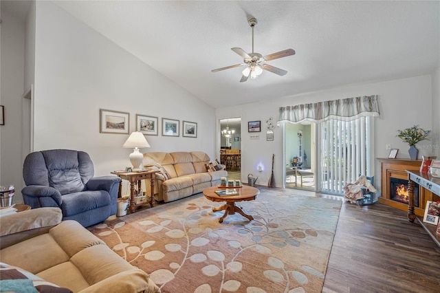 living room featuring a warm lit fireplace, ceiling fan, high vaulted ceiling, and wood finished floors