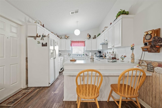 kitchen with white refrigerator with ice dispenser, visible vents, a peninsula, light countertops, and under cabinet range hood