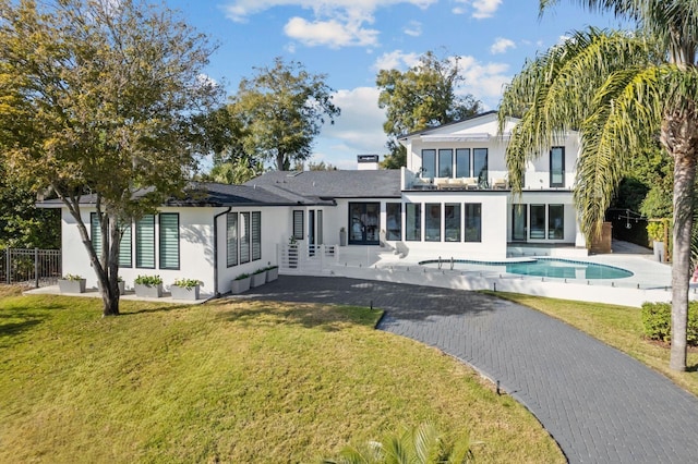 rear view of house featuring a yard, stucco siding, fence, and an outdoor pool