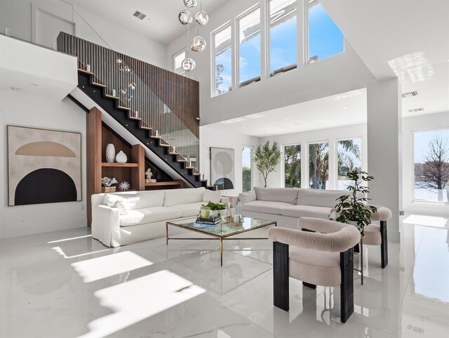 living room with a chandelier, a high ceiling, visible vents, stairs, and marble finish floor